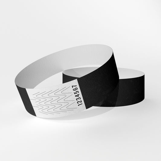 Das Bild zeigt zwei Tyvek-Kontrollarmbänder. Eines über dem anderen. Auf dem oberen Armband ist ein weißes Teil zu sehen, das ein Verschluss aus Klebstoff ist, der beim Abnehmen des Armbands reißt.
