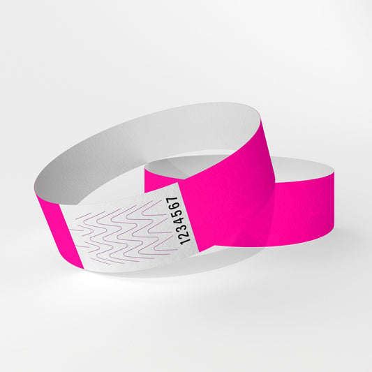 Das Bild zeigt zwei Tyvek-Kontrollarmbänder. Eines über dem anderen. Auf dem oberen Armband ist ein weißes Teil zu sehen, das ein Verschluss aus Klebstoff ist, der beim Abnehmen des Armbands reißt.