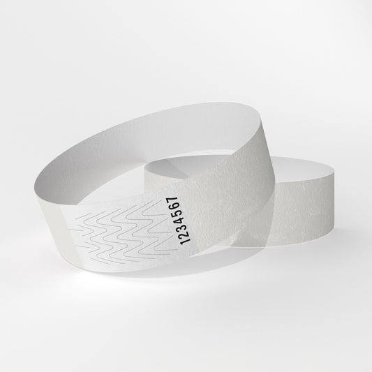 Das Bild zeigt zwei Tyvek-Kontrollarmbänder. Eines über dem anderen. Auf dem oberen Armband ist ein weißes Teil zu sehen, das ein Verschluss aus Klebstoff ist, der beim Abnehmen des Armbands reißt.